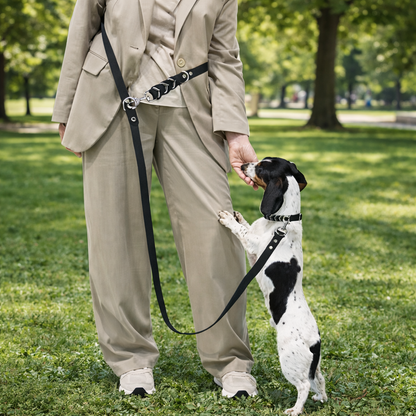 Person in a beige suit standing on grass with a small black and white dog on a leash.